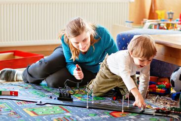 Mother and son playing with racing cars on racetrack,...