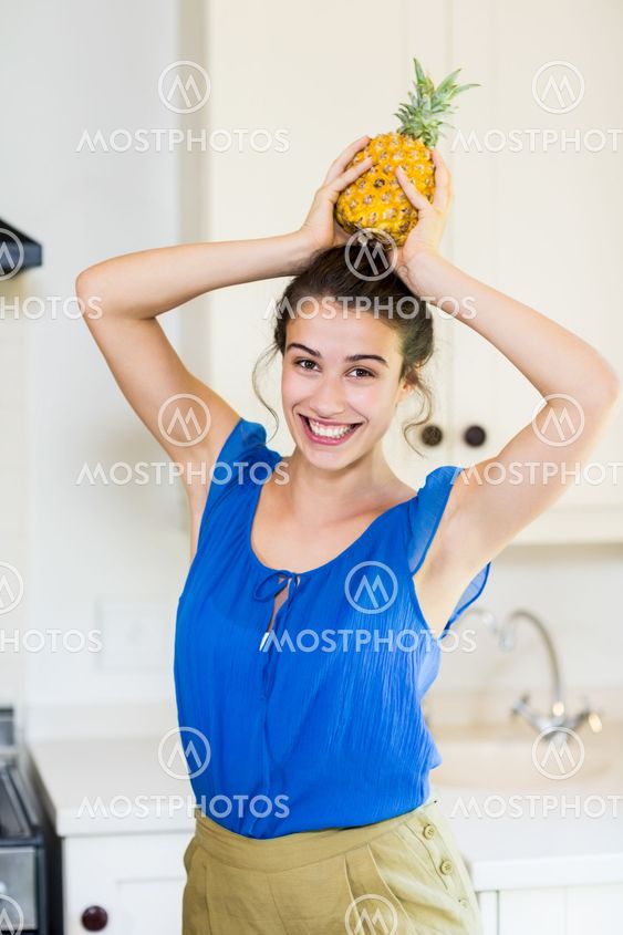 Portrait of young woman carrying pineapple on head