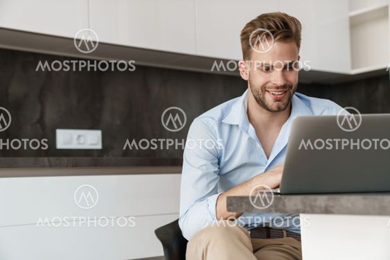 Handsome cheerful guy working with laptop while sitting