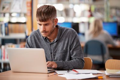 Mature Male Student Working On Laptop In College Library