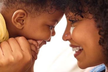 Close Up Of Mother And Baby Daughter Cuddling On Sofa At...