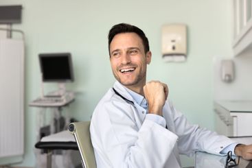 Cheerful handsome male doctor sitting at workplace,...
