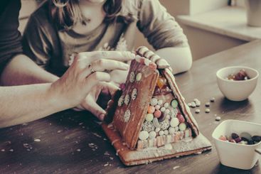 Child and woman decorate a gingerbread house with...