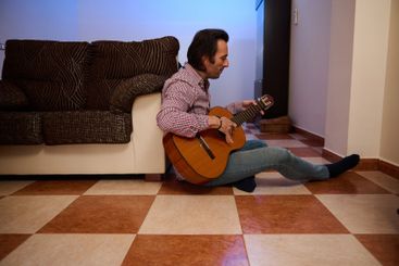 Man playing guitar indoors sitting on the tiled floor...