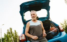 Grey senior sportsman sitting with badminton rackets in...