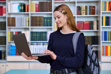 Teenage girl student using laptop, inside high school...