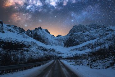 Milky Way over road, snowy mountains at winter starry night
