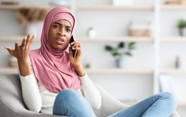 Worried Black Muslim Woman In Hijab Talking On Cellphone...