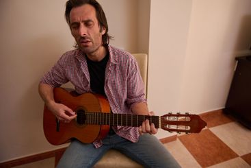 Man emotionally playing an acoustic guitar indoors...