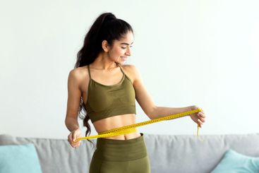 Full length of pretty Indian woman measuring her waist...