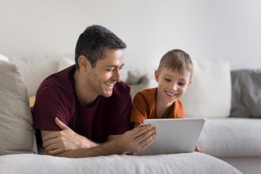Smiling father and son resting on sofa with digital tablet