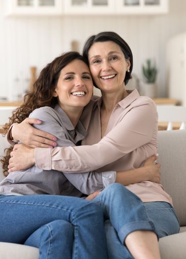 Young woman adult child hug aged mom sitting on sofa