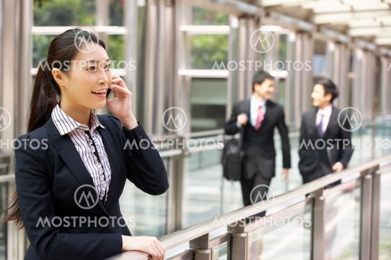 Chinese Businesswoman Outside Office On Mobile Phone With Colleagues In Background