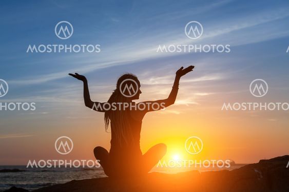 Silhouette young woman practicing yoga on the beach at amazing sunset.