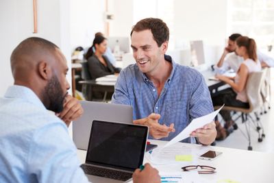 Two men discussing business documents in a busy office