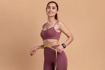 Smiling Young Woman Measuring Waist And Looking At Camera