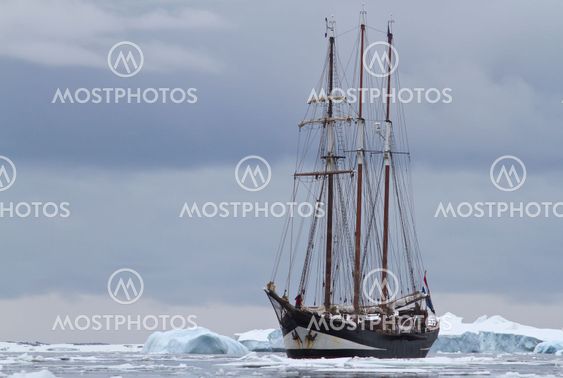 small sailing ship in Antarctic waters between ice floes...