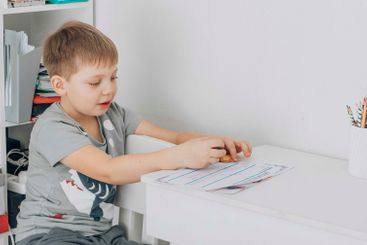 boy concentrating on school work at home, using...