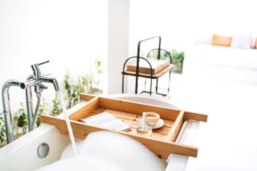 A wooden tray is attached to a bathtub filled with hot...