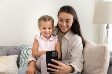 Cheerful young mom holding sweet little girl on lap