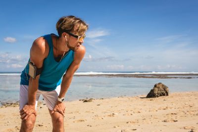 tired sportsman with smartphone armband standing and...