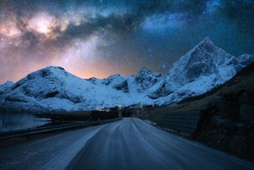 Milky Way over road, snowy mountains at winter starry night