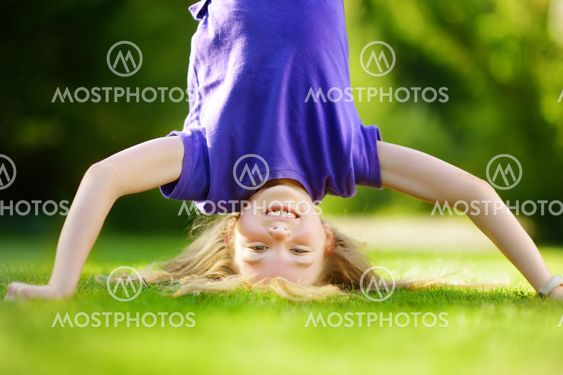 Happy young child playing head over heels on green grass...