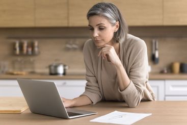 Middle aged woman using notebook at home office in kitchen
