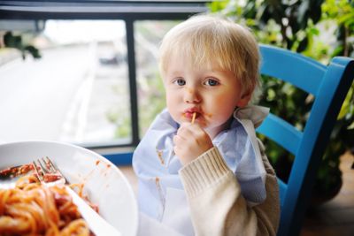 Cute toddler boy eating pasta in Italian indoors restaurant