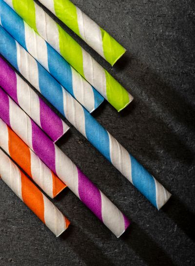 Multicoloured drink straws on dark stone background....