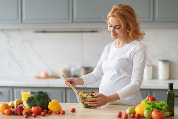 Pregnant woman preparing a fresh salad in a modern...