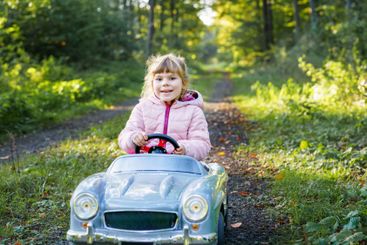 Little preschool girl driving big vintage toy car. Happy...