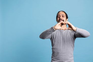 Romantic person showing a heart shape sign against blue...