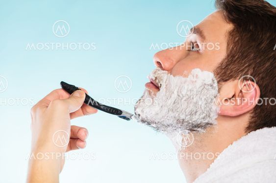 Young man shaving using razor with cream foam.