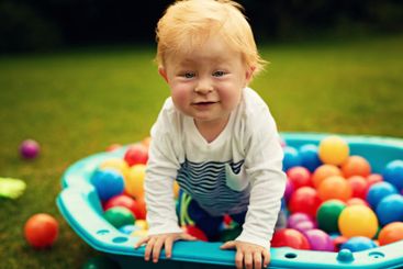 Portrait, colourful and baby in backyard, ball pit and...