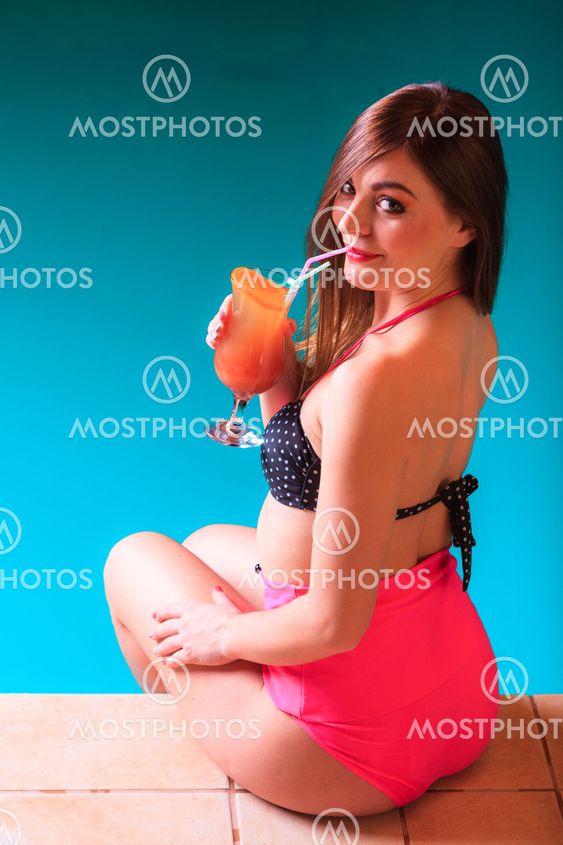 Woman with cocktail drink at swimming pool edge.