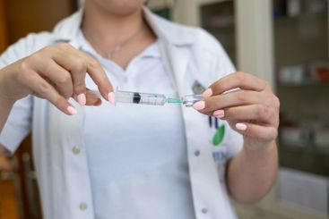 A focused nurse in a white lab coat carefully prepares a...