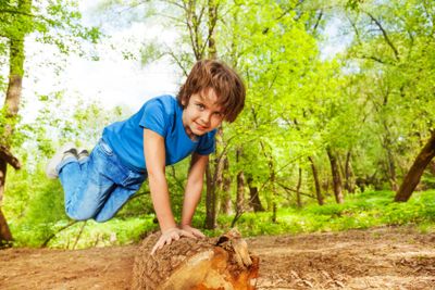 Young boy jumping over the log in summer forest
