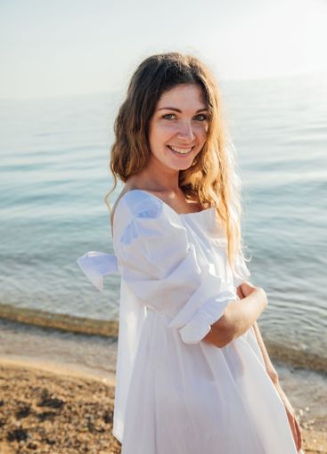 Beautiful woman in white summer dress on sandy beach by...
