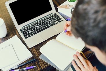 Individual writes notes in a notebook while using a...
