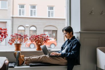 Businessman working on laptop while sitting on window...