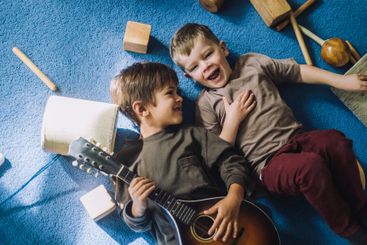 Cheerful boy lying down with male classmate holding...
