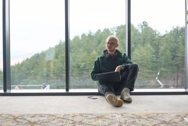 A blonde man sitting on the floor of a modern office,...