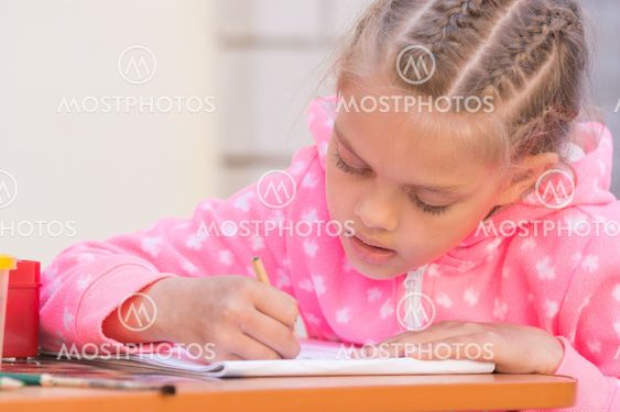 Schoolgirl is drawing in pencil on the album, in the yard