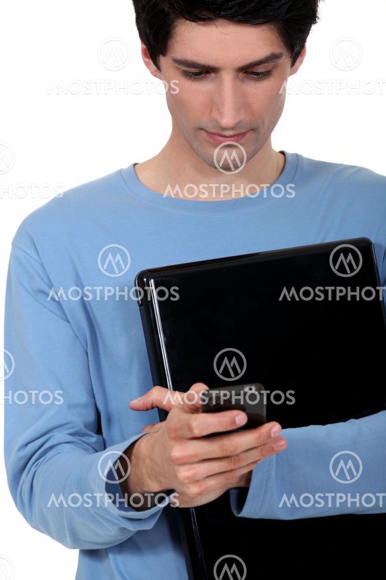 A casual young man with a laptop and a cellphone.