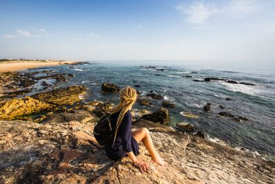 A young woman on the rocks looking at the ocean.