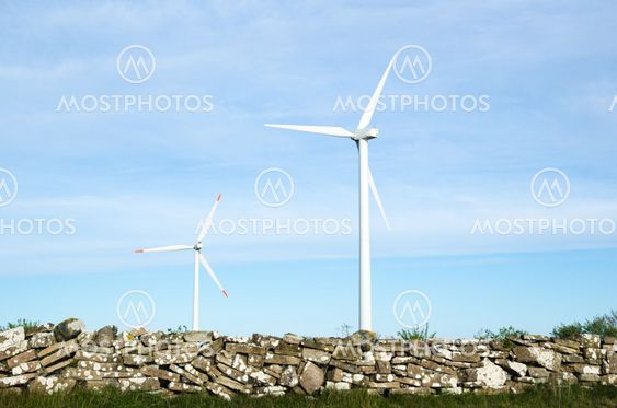 Two wind turbines by an old traditional stonewall at the...