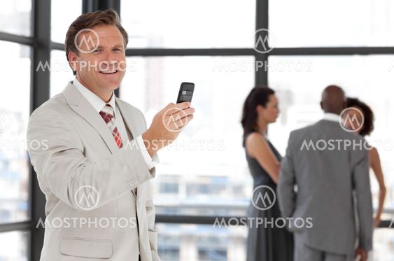 Charismatic businessman holding a phone at workplace with his colleagues