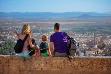 Travelers with kids sit on high wall and enjoy Alhambra...