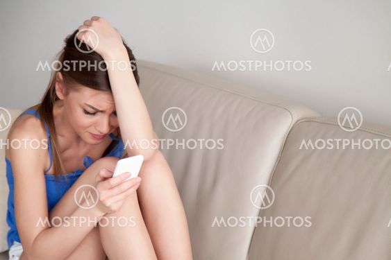 Crying depressed teen girl holding phone, cyberbullying message,
